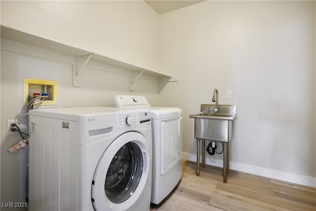 clothes washing area with washer and dryer, baseboards, light wood-style flooring, and laundry area