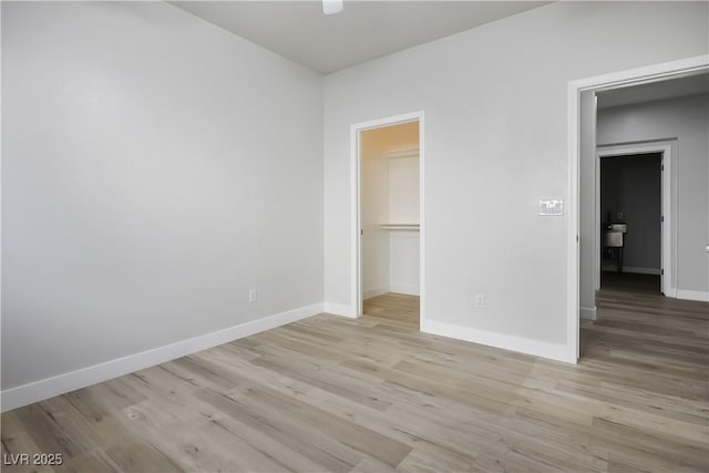 unfurnished bedroom with a spacious closet, a closet, ceiling fan, and light hardwood / wood-style flooring