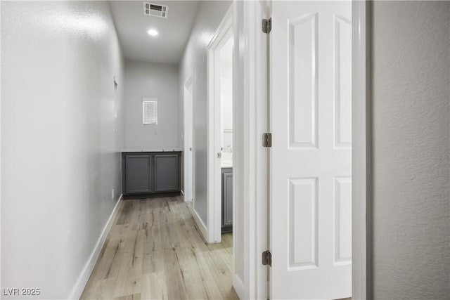 hallway featuring visible vents, light wood-type flooring, and baseboards