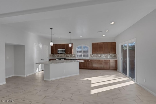 kitchen featuring decorative backsplash, a kitchen island, light stone countertops, and decorative light fixtures