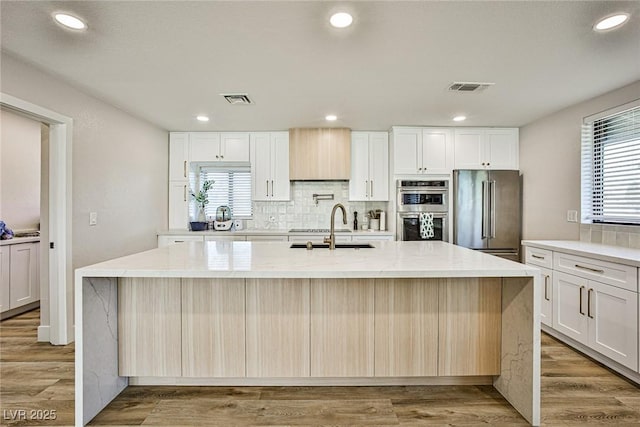 kitchen with light wood-type flooring, stainless steel appliances, a center island with sink, and sink