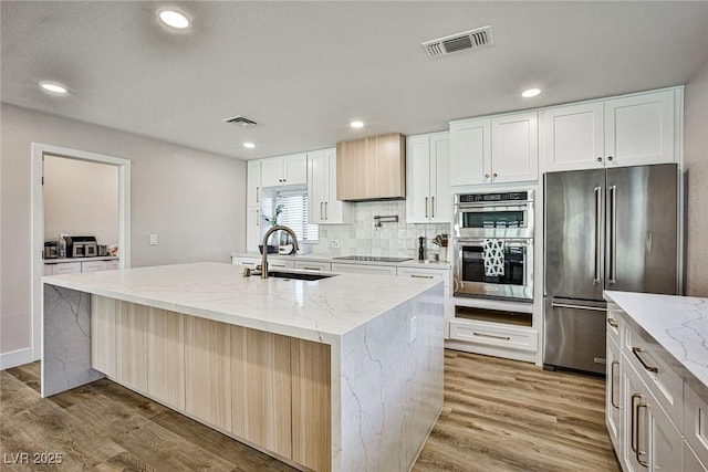 kitchen featuring a kitchen island with sink, sink, light stone counters, white cabinetry, and stainless steel appliances