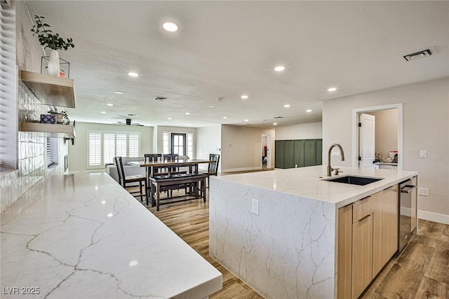 kitchen featuring light stone countertops, sink, light hardwood / wood-style flooring, a large island with sink, and light brown cabinetry