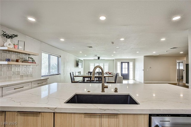 kitchen with dishwasher, light brown cabinets, light stone counters, and sink