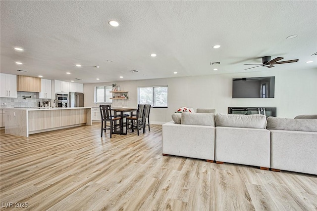 living room featuring ceiling fan, light hardwood / wood-style flooring, a textured ceiling, and sink