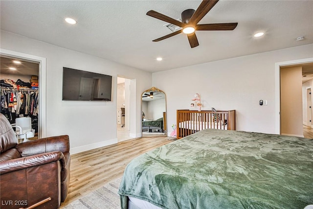 bedroom featuring a closet, a spacious closet, light hardwood / wood-style flooring, and ceiling fan