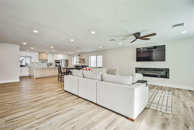 living room featuring ceiling fan, a textured ceiling, and light hardwood / wood-style flooring