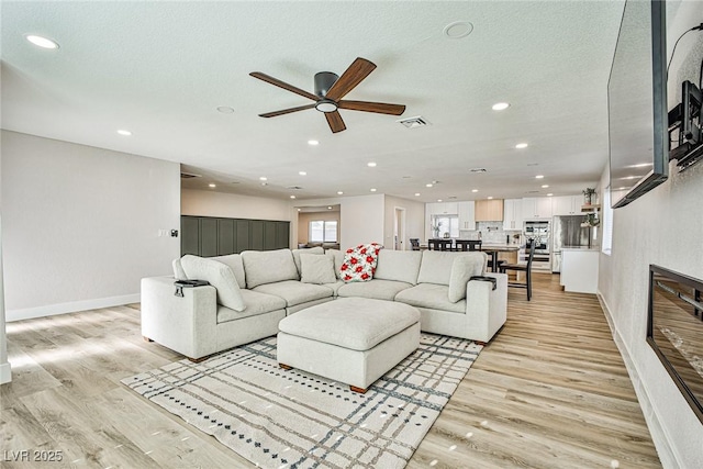 living room with ceiling fan, a textured ceiling, and light wood-type flooring