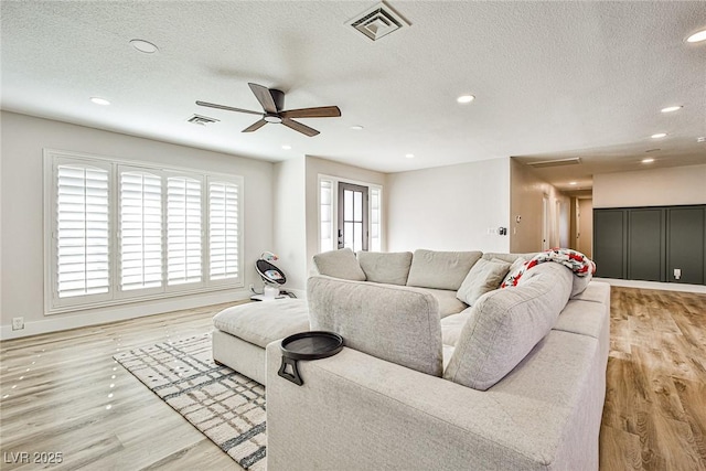 living room featuring a textured ceiling, light wood-type flooring, and ceiling fan