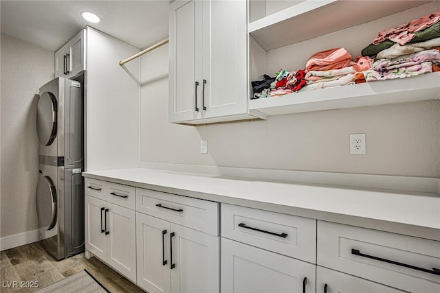 clothes washing area with stacked washer / dryer, cabinets, and light wood-type flooring