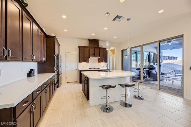 kitchen with a breakfast bar, sink, pendant lighting, and a center island with sink