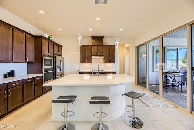 kitchen featuring decorative light fixtures, an island with sink, and stainless steel appliances