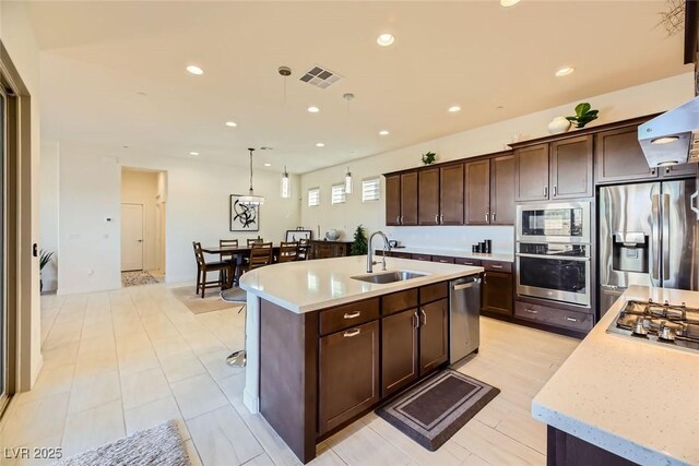 kitchen featuring decorative light fixtures, dishwasher, sink, a kitchen island with sink, and dark brown cabinets