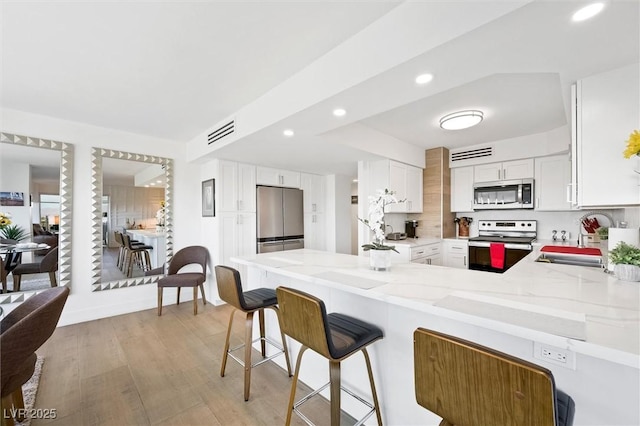 kitchen featuring kitchen peninsula, light stone countertops, stainless steel appliances, sink, and white cabinets