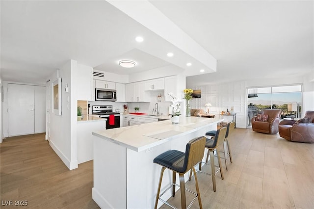 kitchen with sink, stainless steel appliances, kitchen peninsula, a kitchen bar, and white cabinets