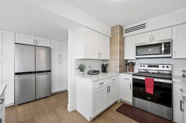 kitchen featuring light wood-type flooring, white cabinetry, backsplash, and appliances with stainless steel finishes