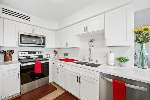 kitchen featuring light stone countertops, appliances with stainless steel finishes, white cabinetry, and sink