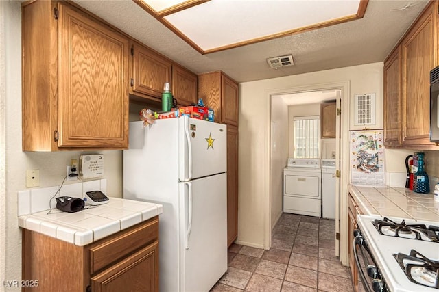 kitchen featuring a textured ceiling, tile countertops, white appliances, and washing machine and dryer