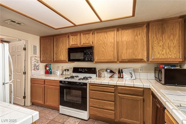 kitchen with tile counters, light tile patterned flooring, and white appliances