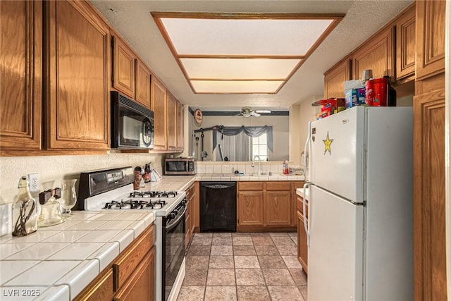 kitchen featuring tile countertops, black appliances, sink, ceiling fan, and a textured ceiling