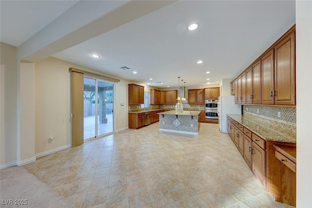 kitchen with hanging light fixtures, white refrigerator, light stone counters, stainless steel double oven, and a kitchen island