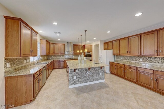 kitchen with stainless steel appliances, sink, decorative light fixtures, wall chimney exhaust hood, and an island with sink