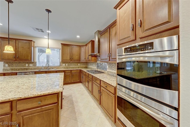 kitchen featuring stainless steel appliances, sink, wall chimney exhaust hood, light stone countertops, and pendant lighting