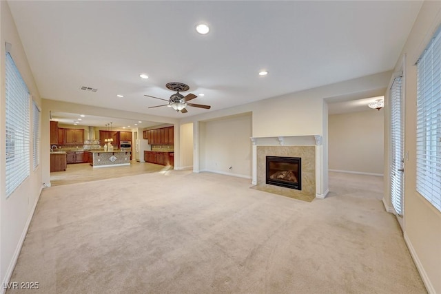 unfurnished living room featuring ceiling fan, light colored carpet, and a fireplace