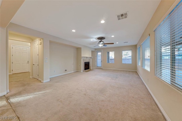 unfurnished living room featuring a high end fireplace, ceiling fan, and light colored carpet