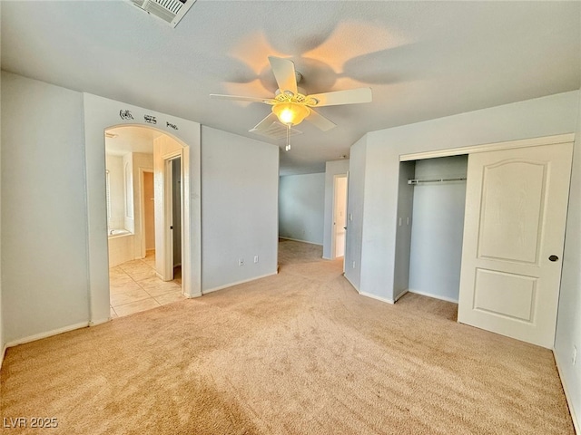 unfurnished bedroom featuring connected bathroom, light colored carpet, a closet, and ceiling fan