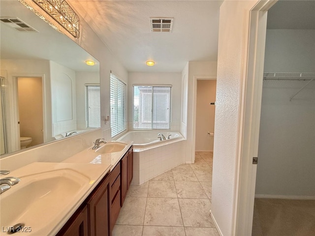 bathroom featuring vanity, tile patterned flooring, toilet, a textured ceiling, and tiled tub