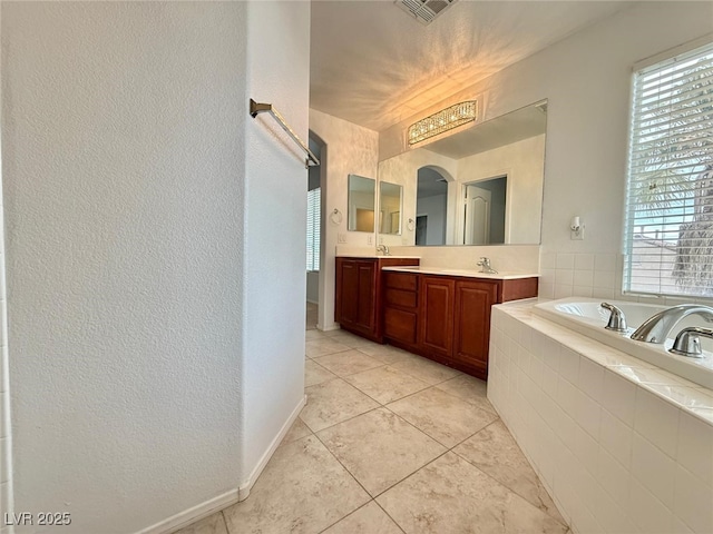 bathroom featuring tile patterned flooring, vanity, and tiled bath