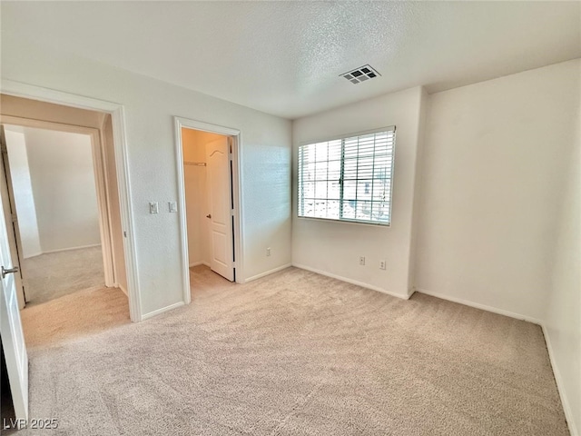 unfurnished bedroom featuring light carpet, a spacious closet, and a textured ceiling