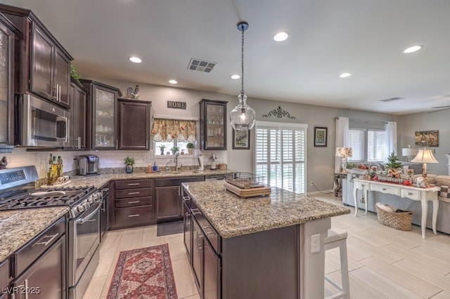 kitchen with appliances with stainless steel finishes, hanging light fixtures, dark brown cabinets, a kitchen breakfast bar, and a center island