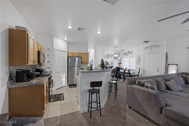 kitchen with tasteful backsplash, a kitchen bar, light tile patterned floors, ceiling fan with notable chandelier, and appliances with stainless steel finishes