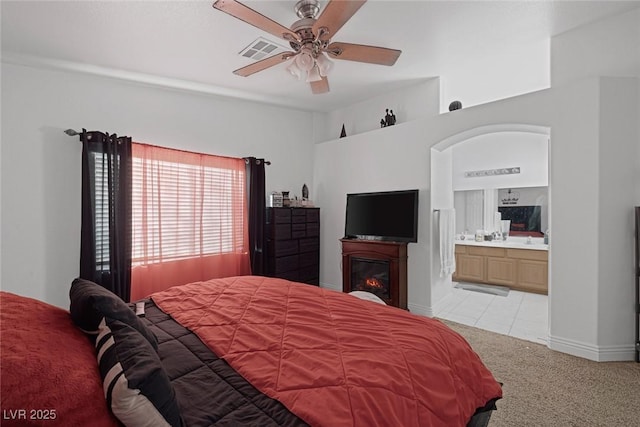 bedroom with ceiling fan, light colored carpet, and ensuite bath