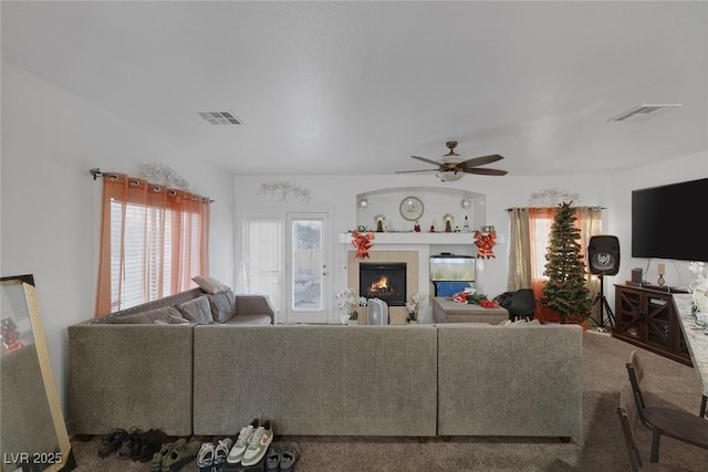 living room with a tile fireplace and ceiling fan