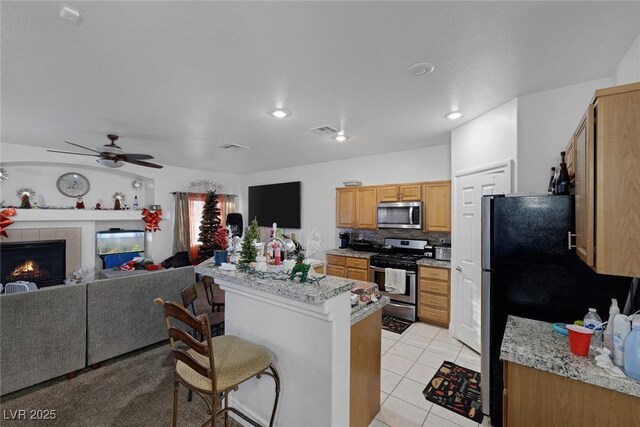 kitchen featuring ceiling fan, stainless steel appliances, a kitchen breakfast bar, a tiled fireplace, and light tile patterned floors