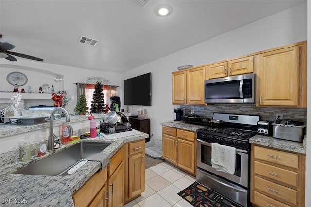 kitchen with light tile patterned flooring, stainless steel appliances, light stone countertops, and sink