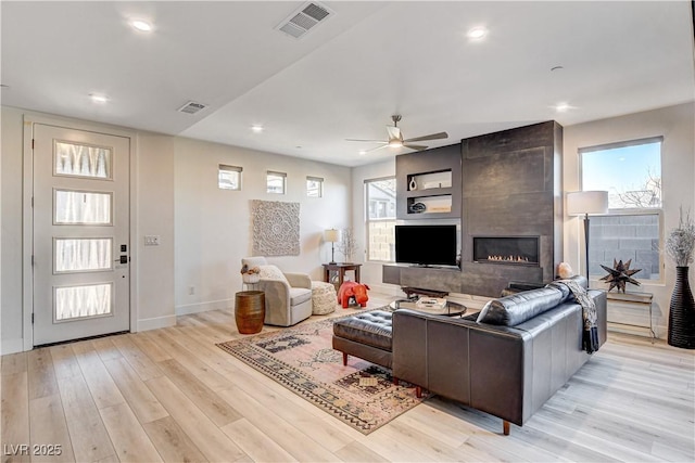 living room with ceiling fan, light hardwood / wood-style floors, and a tiled fireplace