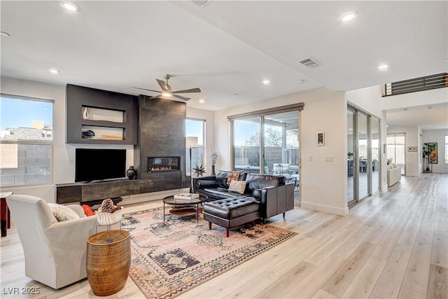 living room with ceiling fan, a large fireplace, and light wood-type flooring