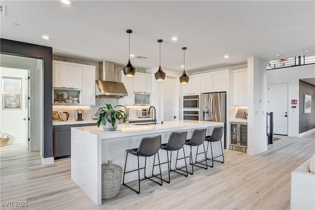 kitchen featuring pendant lighting, white cabinetry, a kitchen island with sink, and wall chimney range hood