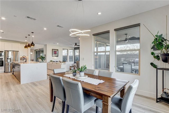 dining room with sink, ceiling fan with notable chandelier, and light wood-type flooring