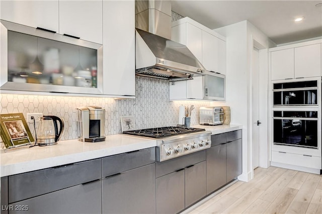 kitchen with gray cabinets, white cabinets, wall chimney exhaust hood, and stainless steel gas cooktop