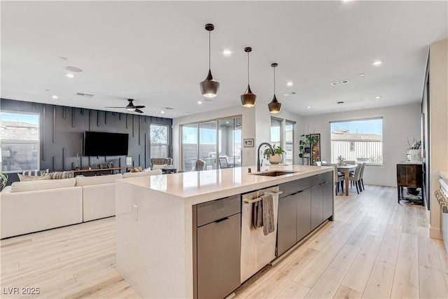 kitchen with stainless steel dishwasher, sink, pendant lighting, light hardwood / wood-style floors, and a large island