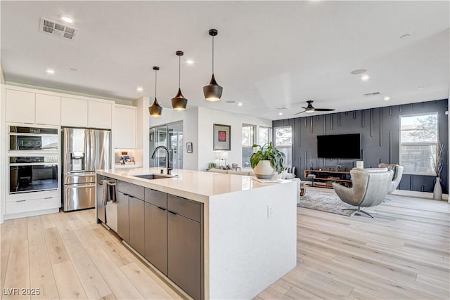 kitchen featuring stainless steel appliances, a spacious island, sink, decorative light fixtures, and white cabinets