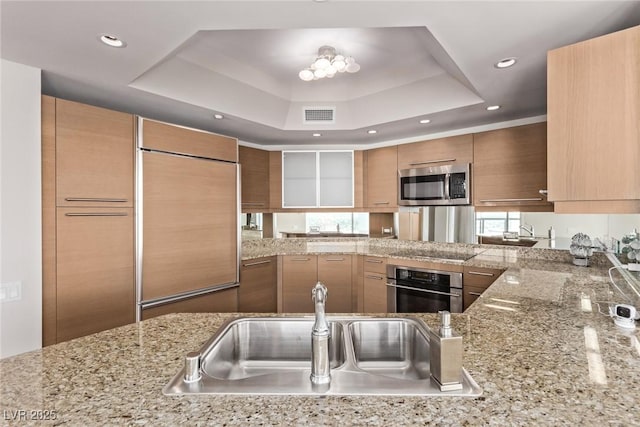 kitchen featuring stainless steel appliances, a tray ceiling, kitchen peninsula, and sink