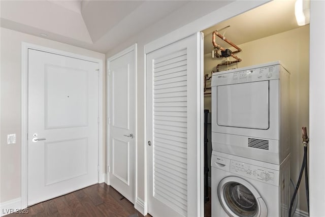 clothes washing area with stacked washer and dryer and dark wood-type flooring