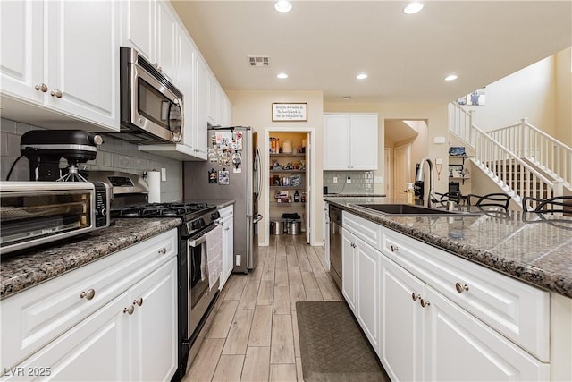 kitchen featuring dark stone counters, sink, tasteful backsplash, white cabinetry, and stainless steel appliances