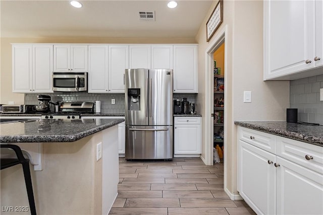 kitchen with decorative backsplash, appliances with stainless steel finishes, dark stone counters, white cabinets, and a kitchen island